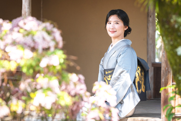 グレーの着物を着て庭の花を見つめる女性の画像